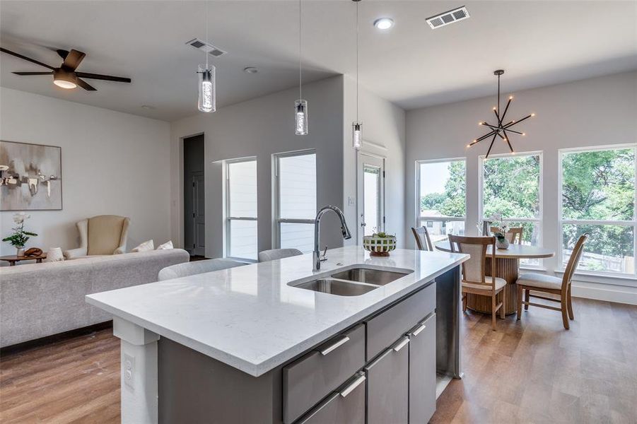 Kitchen with light hardwood / wood-style flooring, ceiling fan with notable chandelier, a center island with sink, sink, and pendant lighting