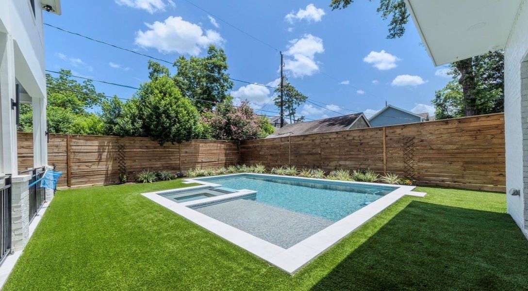 This backyard features a sleek, modern swimming pool with a spa, surrounded by lush artificial turf and a wooden privacy fence, creating a serene outdoor oasis.
