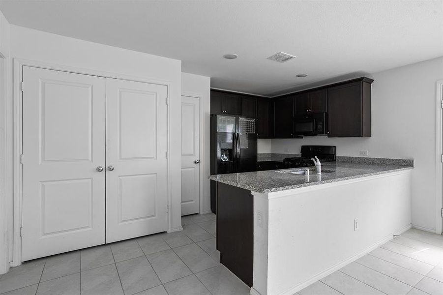 Kitchen with light tile patterned floors, black appliances, light stone counters, a peninsula, and dark brown cabinets