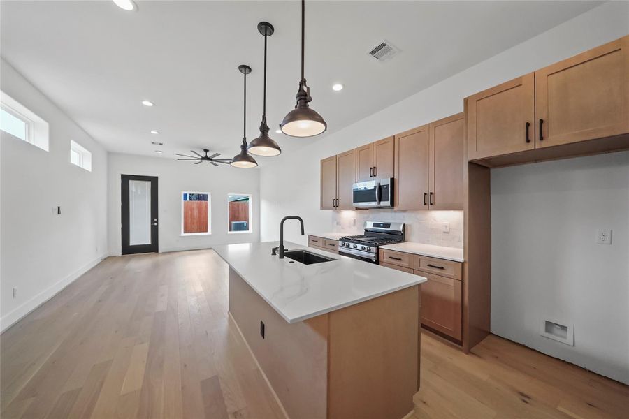 Sleek open-concept kitchen with light wood cabinetry, stainless steel appliances, a central island with sink, and elegant pendant lighting. Enjoy hardwood floors and abundant natural light. Sleek open-concept kitchen with light wood cabinetry, stainless steel appliances, a central island with sink, and elegant pendant lighting. Enjoy hardwood floors and abundant natural light.