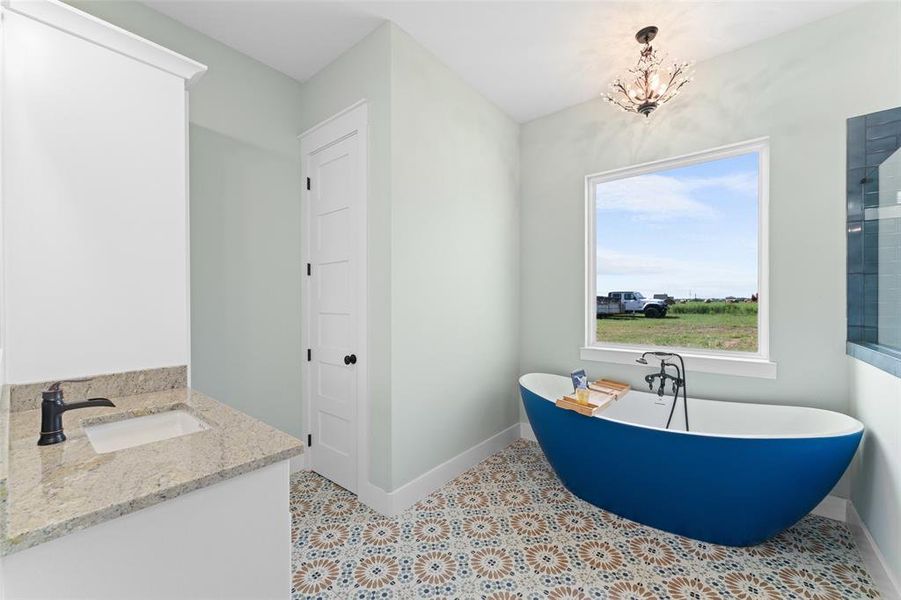 Freestanding blue soaking tub with floor-mounted faucet, complemented by patterned floor tiles