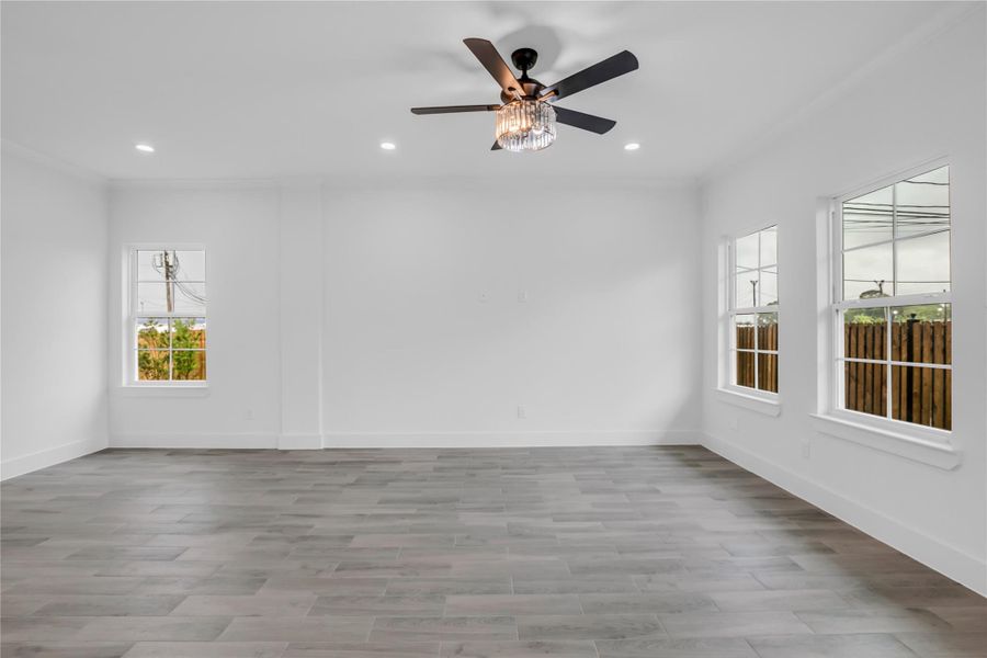 This inviting living room boasts abundant natural light, elegant wood-style flooring, and a modern ceiling fan, offering a perfect blend of comfort and style for your dream home.