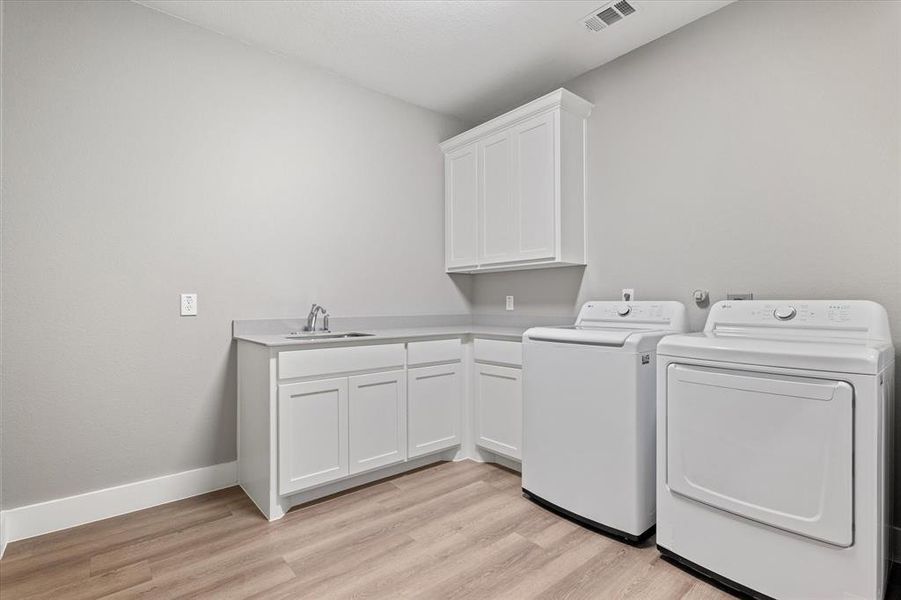 Laundry room featuring sink, washer and dryer, light hardwood / wood-style floors, and cabinets