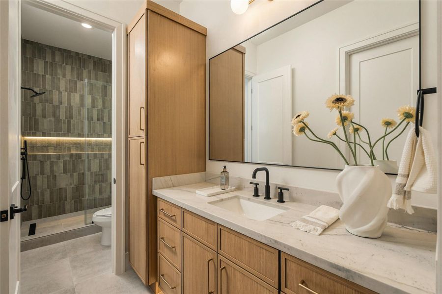 The secondary bath is finished with Mount Blanc Quartzite countertops, full-height designer tile, and a frameless glass shower, bringing the same level of finish found throughout the home into the guest accommodations.
