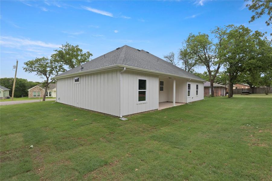 Rear exterior featuring white vertical siding, a covered patio, a dark shingle roof, and a spacious lawn Rear exterior featuring white vertical siding, a covered patio, a dark shingle roof, and a spacious lawn