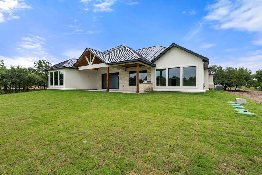 A striking modern farmhouse with expansive rear windows opens to a lush green yard.