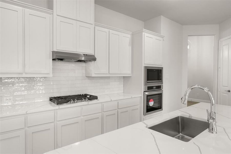 Kitchen with stainless steel appliances, under cabinet range hood, white cabinetry, decorative backsplash, and light stone countertops Kitchen with stainless steel appliances, under cabinet range hood, white cabinetry, decorative backsplash, and light stone countertops