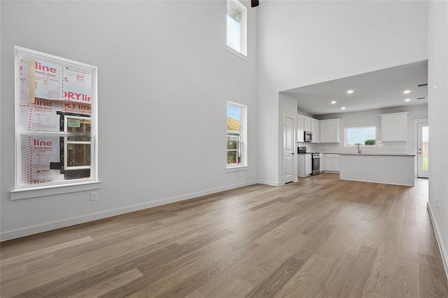 Unfurnished living room with light wood-style flooring, a high ceiling, a sink, baseboards, and recessed lighting Unfurnished living room with light wood-style flooring, a high ceiling, a sink, baseboards, and recessed lighting