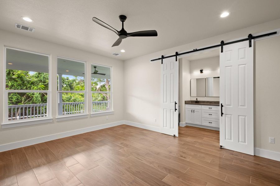 Unfurnished bedroom featuring a barn door, multiple windows, light wood-style floors, connected bathroom, and recessed lighting