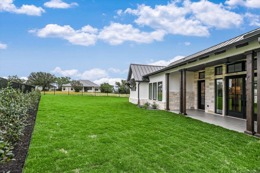 Spacious rear yard featuring manicured lawn, dark metal fencing, and established shrubbery