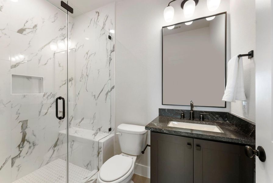 Third en-suite bath features a marble look shower surround, black fixtures, and a streamlined vanity. Its finish level supports the home’s overall custom feel.