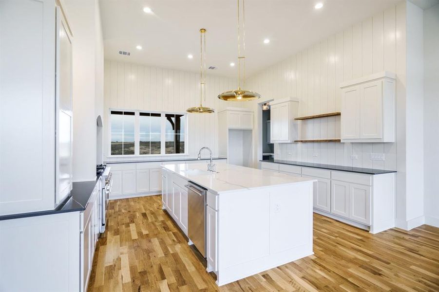 Kitchen with a kitchen island with sink, sink, white cabinets, light hardwood / wood-style floors, and hanging light fixtures