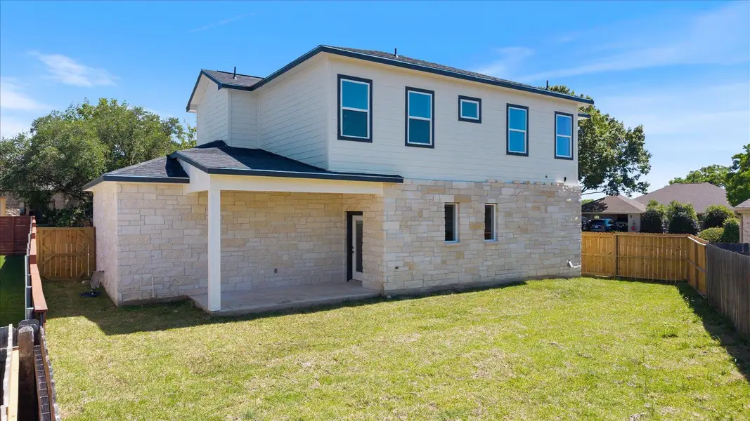 A newly constructed residence combines stone and siding, complemented by a neatly fenced yard and concrete patio.