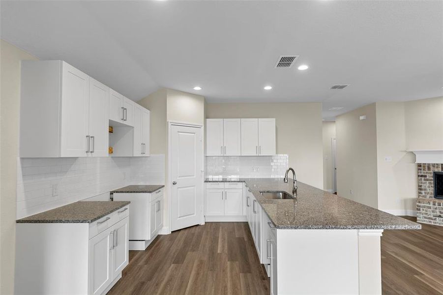Modern kitchen featuring white shaker cabinetry, speckled countertops, a subway tile backsplash, a kitchen island with an undermount sink and gooseneck faucet, and wood-finish flooring