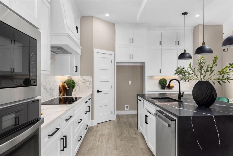 Kitchen with appliances with stainless steel finishes, dark stone counters, sink, white cabinets, and hanging light fixtures