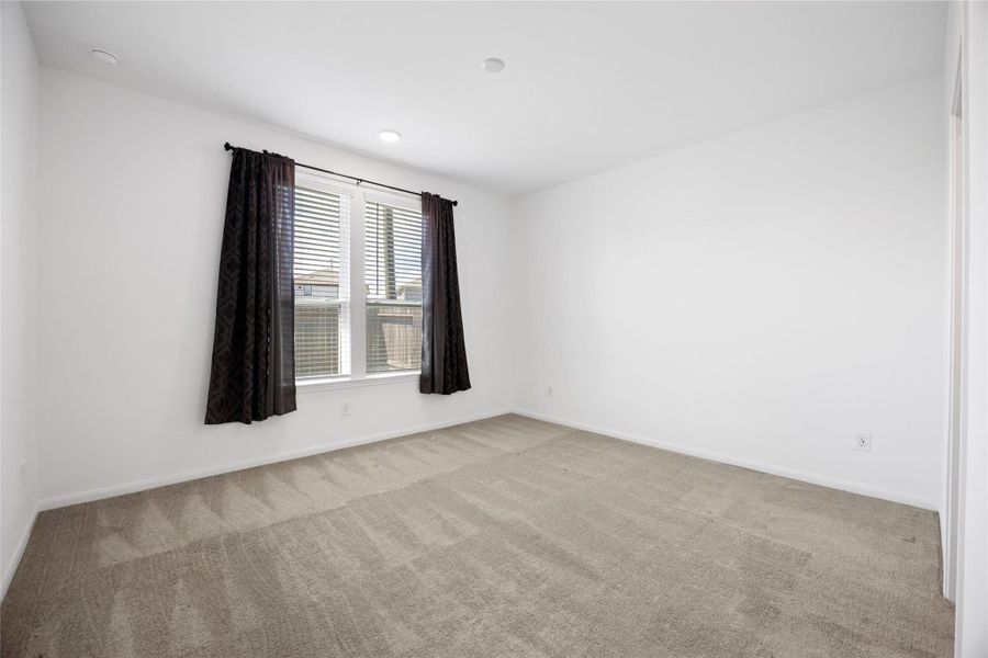 clean, neutral-color walls and carpet, with a large window that provides ample natural light, complemented by dark curtains. It's a bright and versatile space suitable for a bedroom or office.