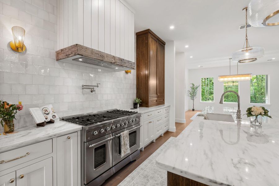 The professional-grade range is accented by a custom vent hood and pot filler, while brass hardware and sconces add warmth and detail.