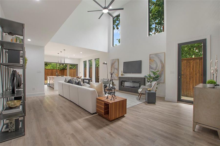 Living room with light wood-type flooring, a towering ceiling, and ceiling fan with notable chandelier