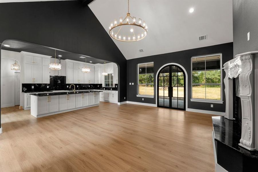 Unfurnished living room featuring arched walkways, light wood-type flooring, a chandelier, high vaulted ceiling, and recessed lighting