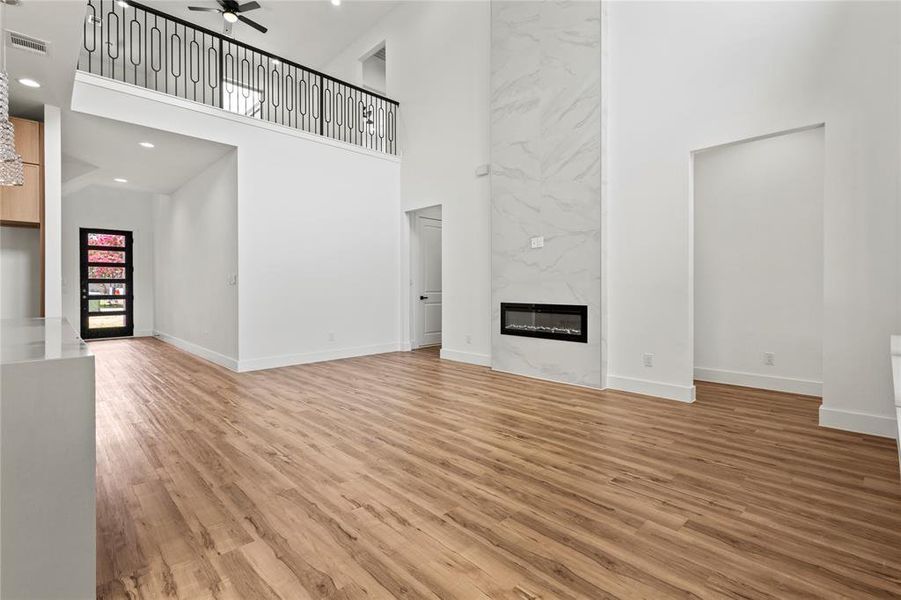 Unfurnished living room with a high ceiling, a high end fireplace, ceiling fan, and light hardwood / wood-style floors