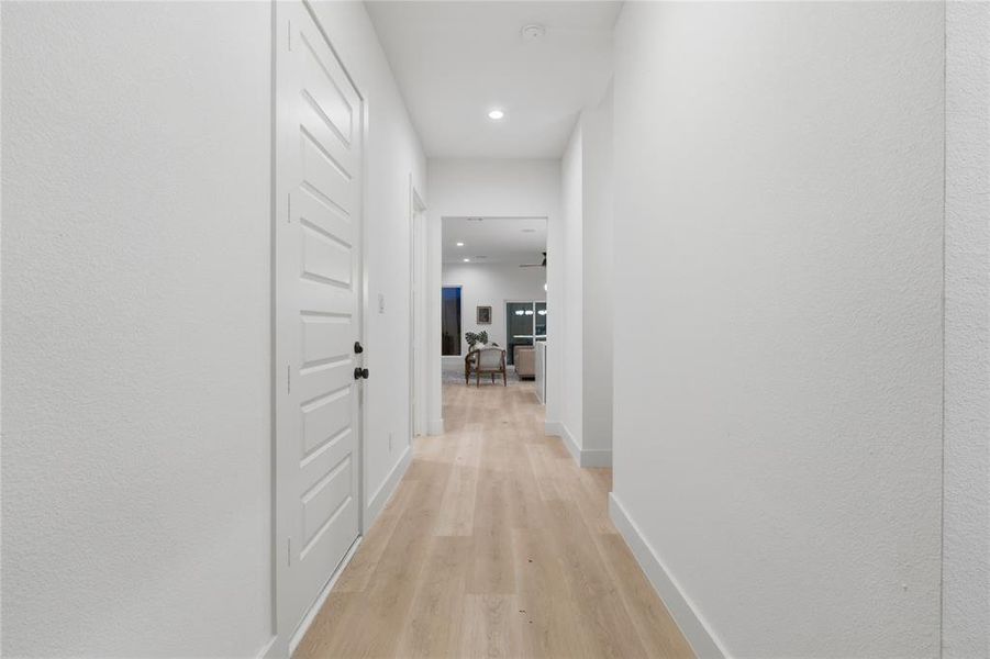 Streamlined hallway featuring light wood-finish flooring, recessed lighting, and crisp white walls