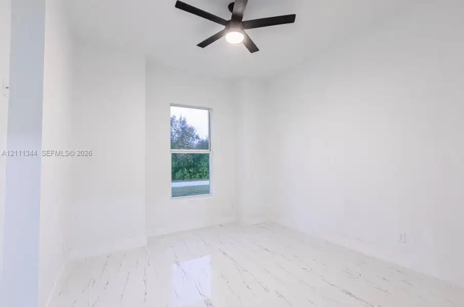 Room featuring white stone-finish tile flooring, a dual-pane window, and a matte black ceiling fan with integrated lighting Room featuring white stone-finish tile flooring, a dual-pane window, and a matte black ceiling fan with integrated lighting