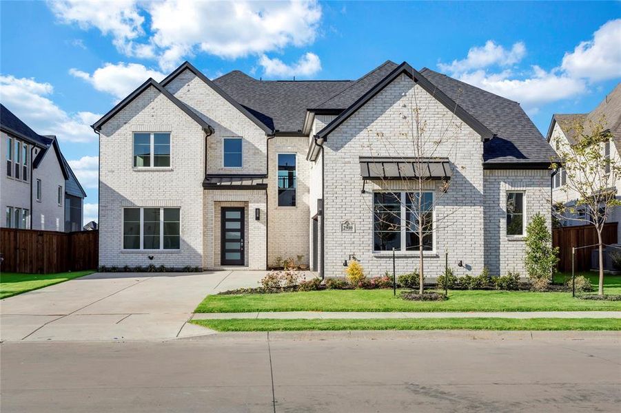 French country style house featuring brick siding, roof with shingles, and concrete driveway
