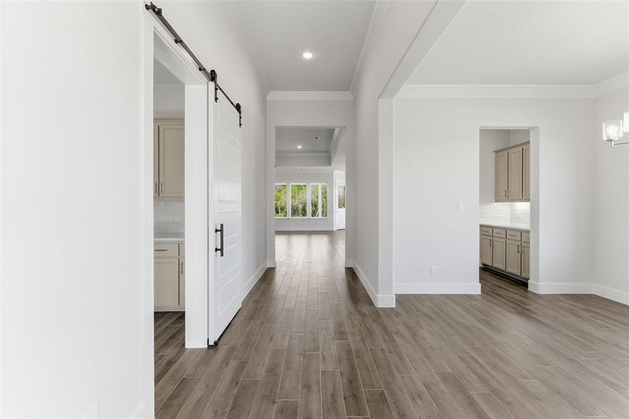 Hall with a barn door, dark wood-style flooring, recessed lighting, and ornamental molding