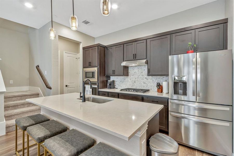 Kitchen featuring light wood-type flooring, stainless steel appliances, sink, tasteful backsplash, and a kitchen bar