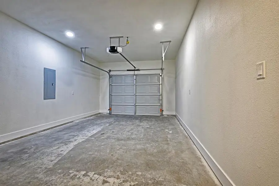 Garage featuring electric panel, a textured wall, recessed lighting, and a garage door opener Garage featuring electric panel, a textured wall, recessed lighting, and a garage door opener
