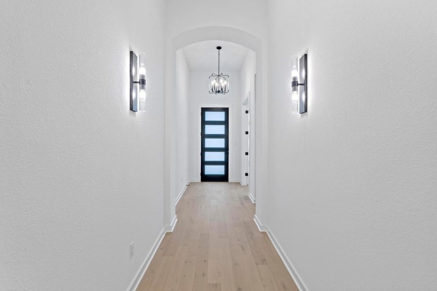 Corridor with arched walkways, light wood-style floors, and a chandelier