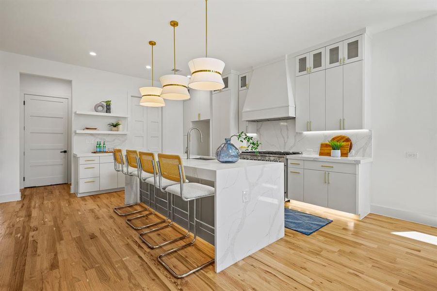 Kitchen featuring a kitchen island with sink, light hardwood / wood-style flooring, custom range hood, and white cabinetry