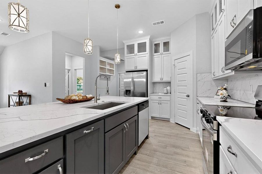 Kitchen with stainless steel appliances, glass insert cabinets, light stone counters, backsplash, and light wood-style floors Kitchen with stainless steel appliances, glass insert cabinets, light stone counters, backsplash, and light wood-style floors