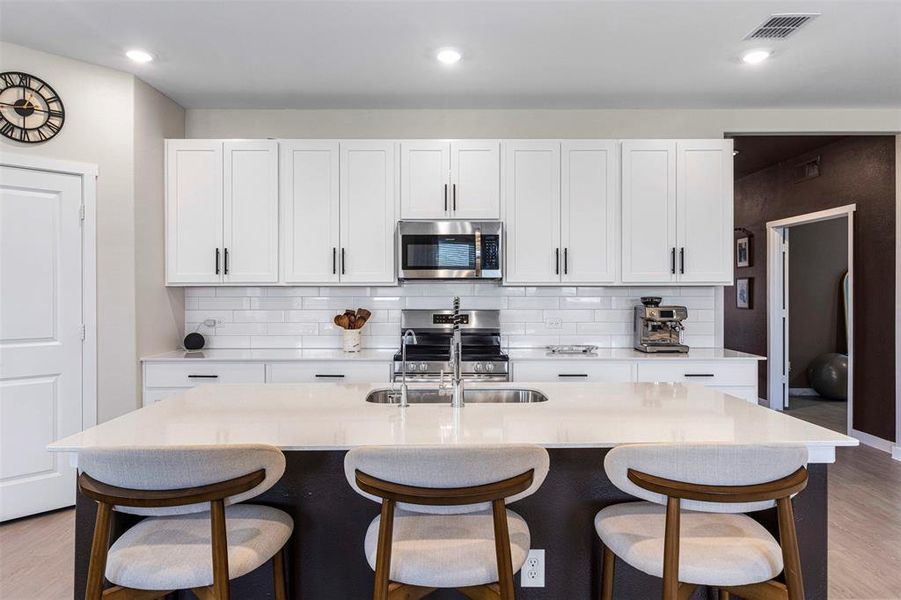 Kitchen featuring an oversized island with seating, white shaker cabinetry, stainless steel appliances, white subway tile backsplash, and recessed lighting Kitchen featuring an oversized island with seating, white shaker cabinetry, stainless steel appliances, white subway tile backsplash, and recessed lighting