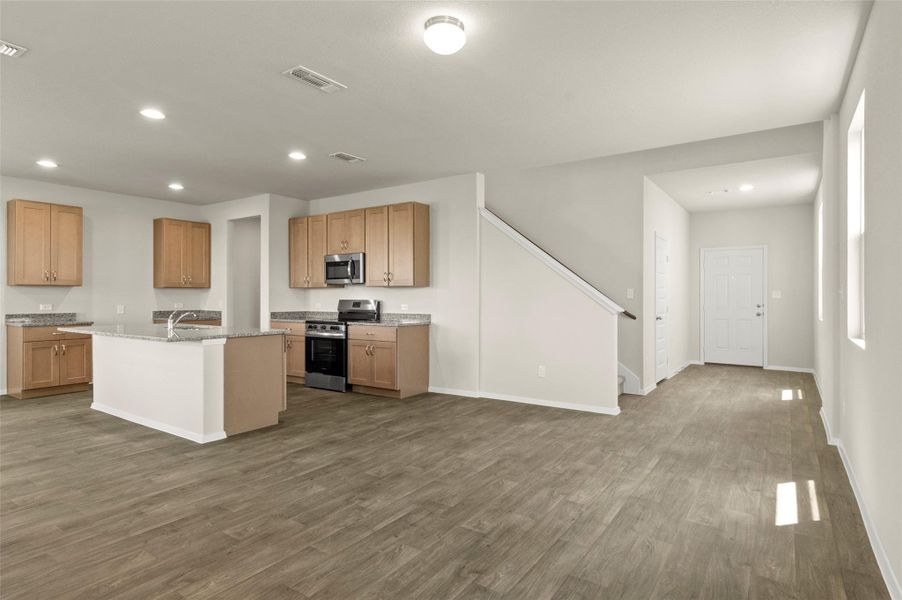 Kitchen with stainless steel appliances, recessed lighting, dark wood finished floors, a kitchen island with sink, and light stone countertops