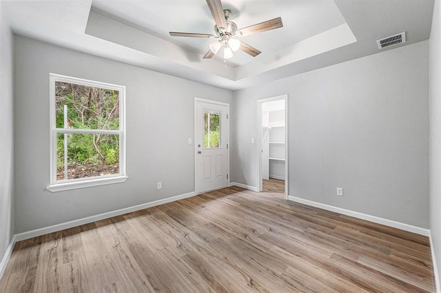 Empty room featuring a tray ceiling, baseboards, a ceiling fan, and light wood-type flooring Empty room featuring a tray ceiling, baseboards, a ceiling fan, and light wood-type flooring