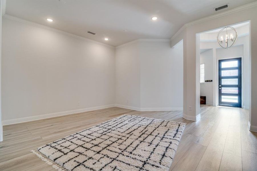 Foyer entrance featuring light wood finished floors, visible vents, a notable chandelier, and ornamental molding Foyer entrance featuring light wood finished floors, visible vents, a notable chandelier, and ornamental molding
