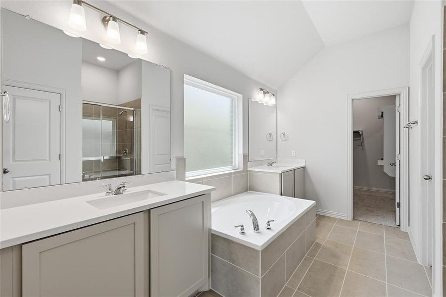 Full bath featuring two vanities, light tile patterned flooring, a spacious closet, a garden tub, and a shower stall