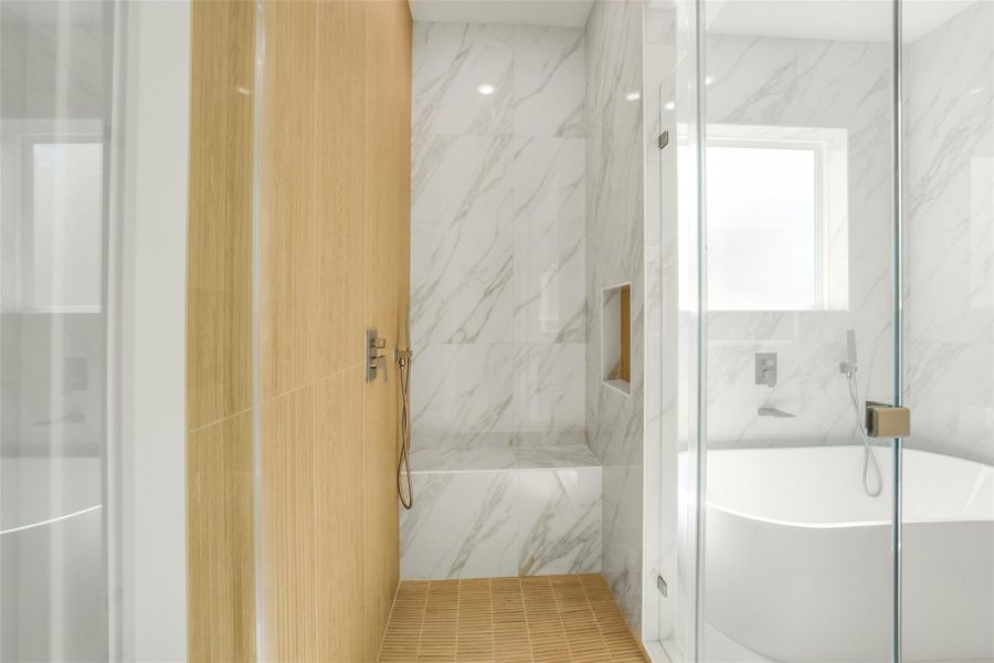 This photo showcases a modern bathroom featuring a sleek, glass-enclosed shower with wooden accents, elegant marble walls, and a stylish freestanding bathtub under a bright window, offering a luxurious and serene atmosphere.