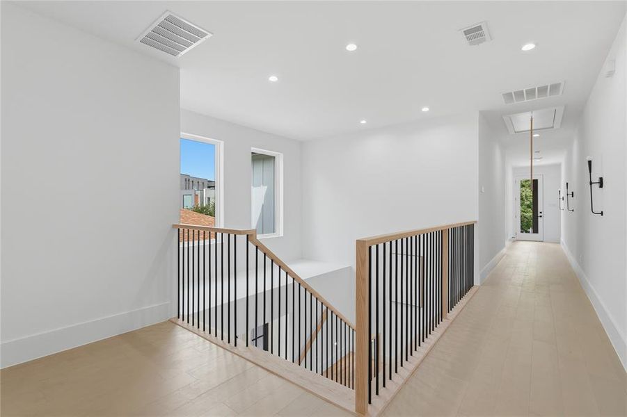 Modern landing featuring a wood-finish flooring, recessed lighting, and a contemporary staircase with black metal balusters and a light wood handrail