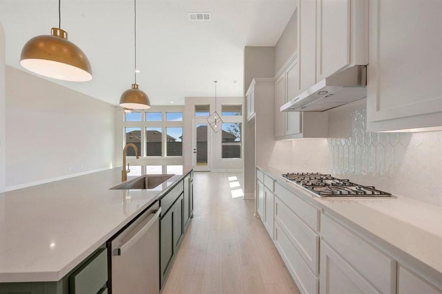 Kitchen featuring a large central island with an undermount sink and brushed brass faucet, white shaker-style cabinetry, a gas cooktop, and a decorative tile backsplash