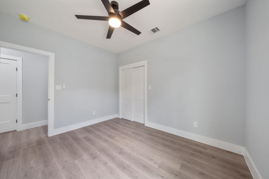 Neutral-toned room featuring wood-finish flooring, light gray walls, a ceiling fan with integrated lighting, white baseboards, and a white bi-fold closet door