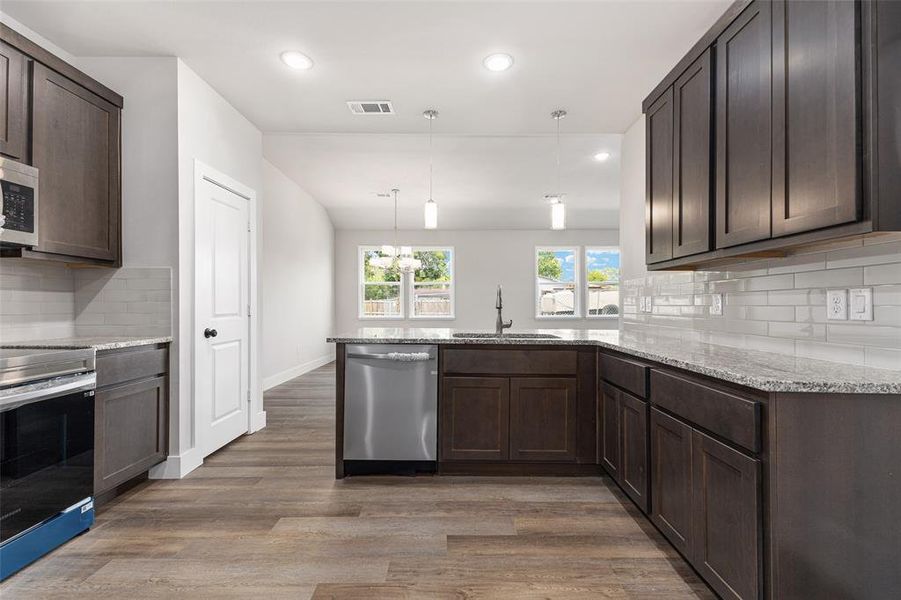 Kitchen with hardwood / wood-style floors, pendant lighting, appliances with stainless steel finishes, decorative backsplash, and kitchen peninsula