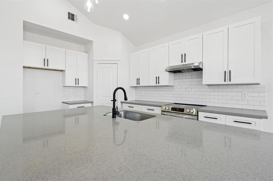 This is a modern, bright kitchen featuring white cabinetry, stainless steel appliances, a subway tile backsplash, and a spacious grey countertop with a black faucet.