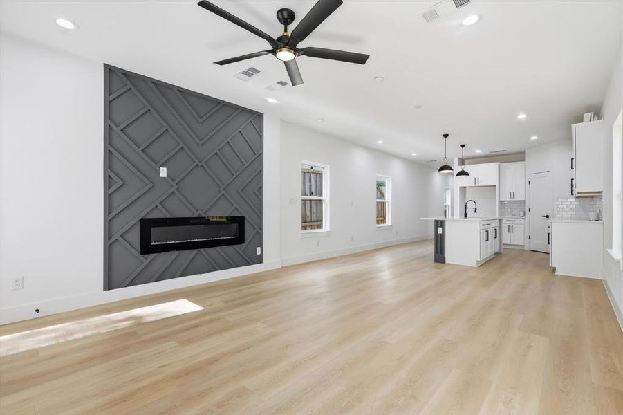 Unfurnished living room with recessed lighting, light wood-style flooring, a ceiling fan, a fireplace, and an accent wall