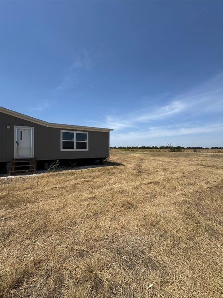 An expansive open pasture surrounds the structure under a clear blue sky.