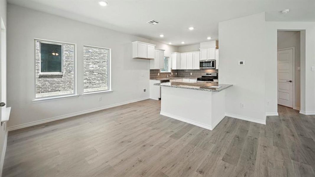 Kitchen featuring white cabinets, light stone countertops, decorative backsplash, a peninsula, and stainless steel appliances