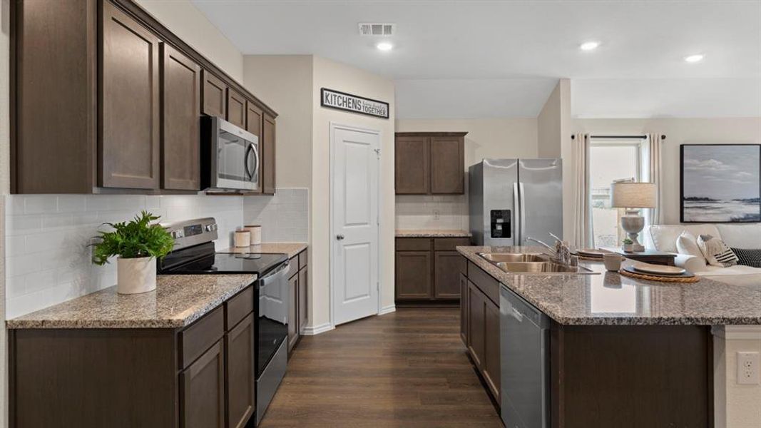 Kitchen with dark wood finish cabinets, stainless steel appliances, backsplash, an island with sink, and dark wood-style floors