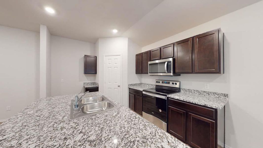 Kitchen featuring a stainless steel double sink, granite countertops, dark wood-finish cabinetry, and stainless steel appliances including an oven and microwave