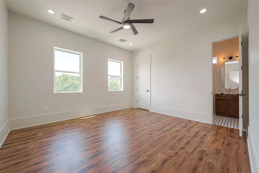 This is a bright, spacious room with hardwood flooring, two windows providing natural light, a ceiling fan, and recessed lighting. It also features a doorway leading to a bathroom with a visible vanity. This is a bright, spacious room with hardwood flooring, two windows providing natural light, a ceiling fan, and recessed lighting. It also features a doorway leading to a bathroom with a visible vanity.